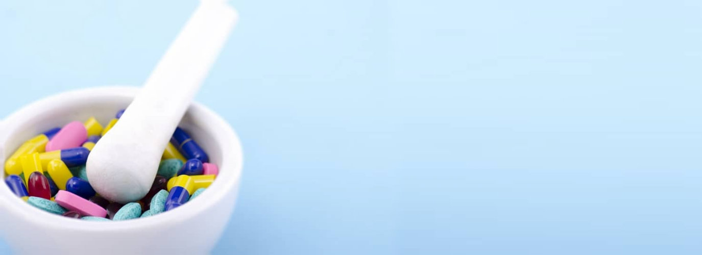 Assorted tablets, pills and capsules inside a white mortar with pestle ite background