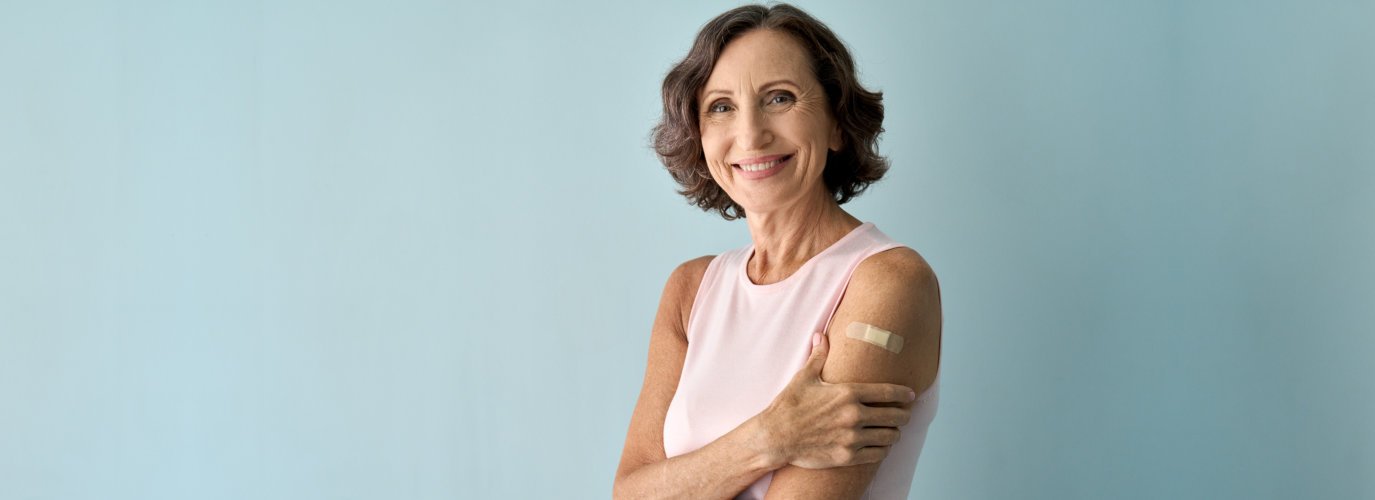 Smiling older senior happy woman showing bandage after getting vaccination.